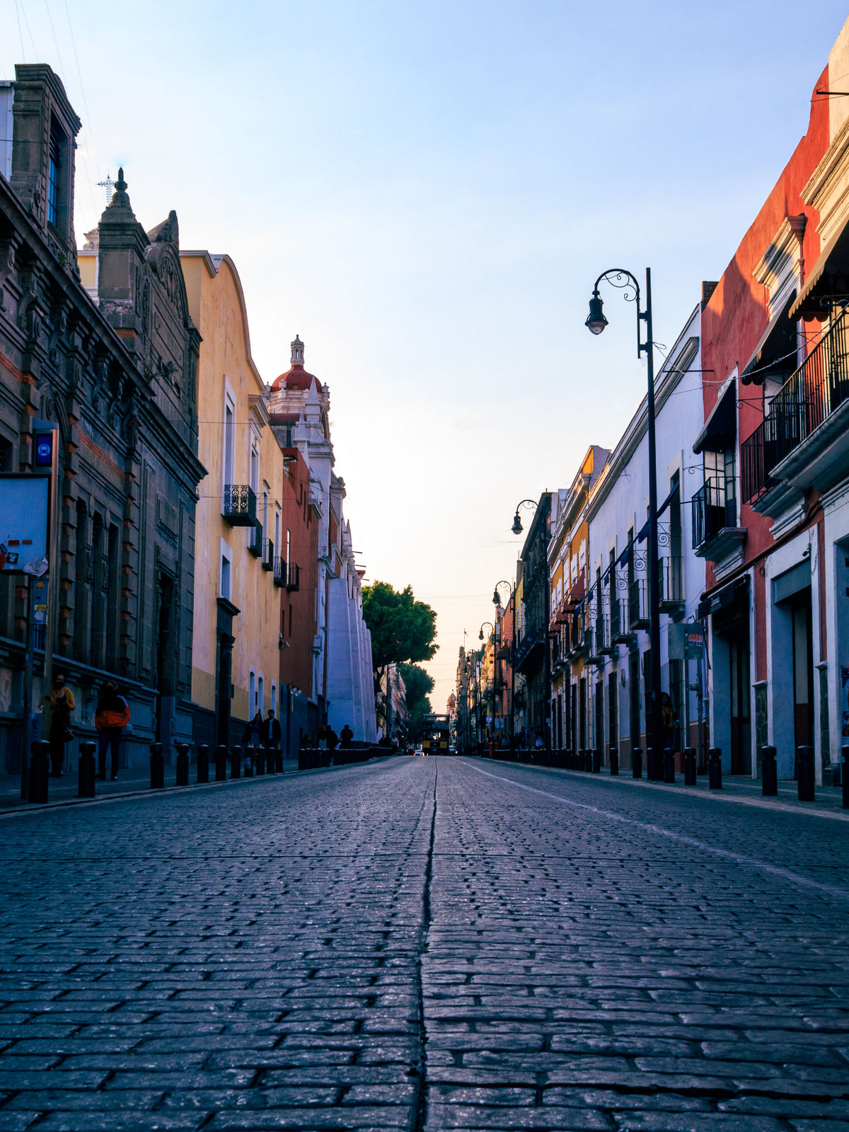 Una calle empedrada que se extiende a lo lejos entre edificios coloniales de colores bajo un cielo azul despejado.
